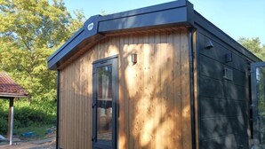 Una pequeña cabaña de madera con techo negro, puerta de vidrio y una ventana pequeña.