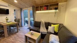 Una sala de estar moderna con techo de madera, un sofá gris con una toalla blanca, una mesita de madera y un televisor montado en la pared.