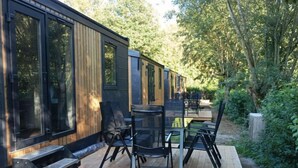 Una terraza moderna al aire libre con suelo de madera, sillas de metal y una mesa de vidrio.