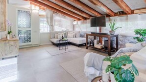 A spacious loft-style living room with exposed wooden beams, a large window with curtains, a sofa, a coffee table, and a flat-screen TV. - Vacation home Serena by Interhome (Rio Marina)