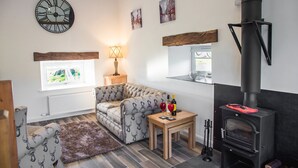 A cozy living room with a sofa, a wooden table with wine glasses, a fireplace, and a clock on the wall. - The Hidden Place (Penrith)