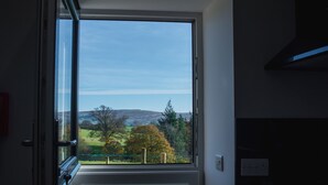 A room with a large window offering a view of a green landscape with trees and hills. - The Hidden Place (Penrith)