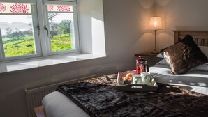 A bedroom with a bed, a tray with breakfast items, a lamp, and a window with a view of greenery. - The Hidden Place (Penrith)