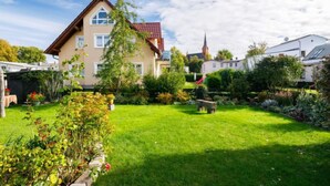 A two-story house with a red-tiled roof, a visible chimney, and a small garden with a lawn and various plants. - Schneider by Interhome (Zinnowitz)