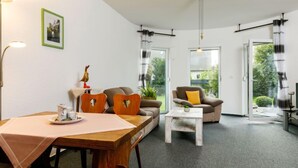 A modern living room with a wooden dining table, a sofa, and a chair. There is a small table with a lamp and a picture frame on the wall. - Schneider by Interhome (Zinnowitz)
