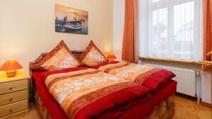 Een hotelkamer met een bed, twee bedlampen, een raam met gordijnen, een radiator en een schilderij aan de muur.