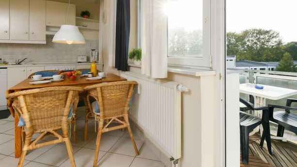 A kitchen with a dining table and chairs, a window with curtains, and a view of the outside. - Zur Düne II by Interhome (Zinnowitz)