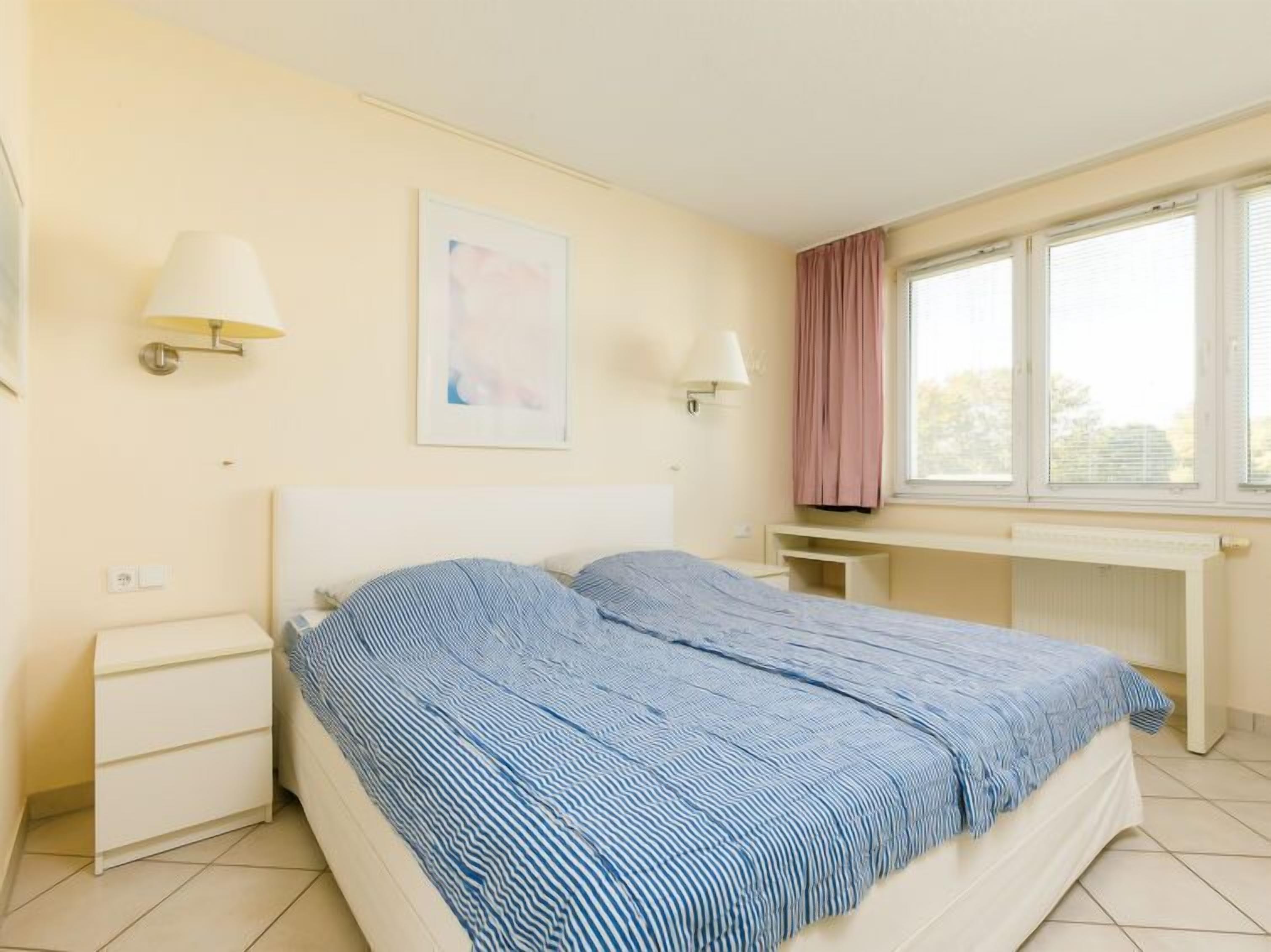 A bedroom with a bed, bedside tables, a desk, and a window with curtains.