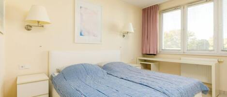 A bedroom with a bed, bedside tables, a desk, and a window with curtains.