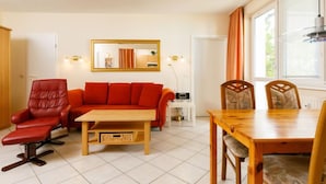 A living room with a red sofa, a wooden coffee table, a red armchair, a wooden dining table with chairs, a mirror, and a window with curtains. - Zur Düne I by Interhome (Zinnowitz)