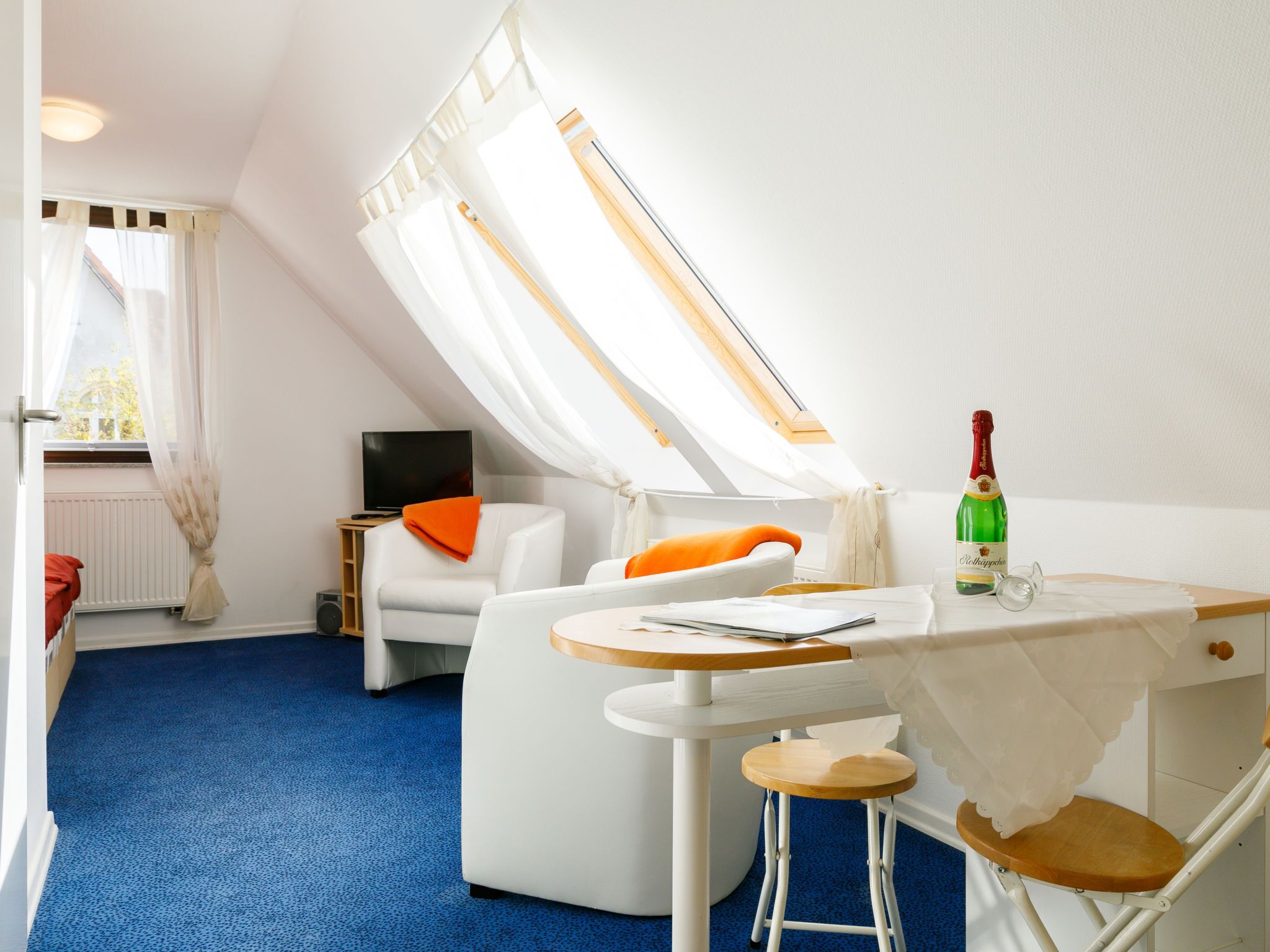 A cozy room with a white sofa, a small table with a bottle of champagne, and a TV on a stand.