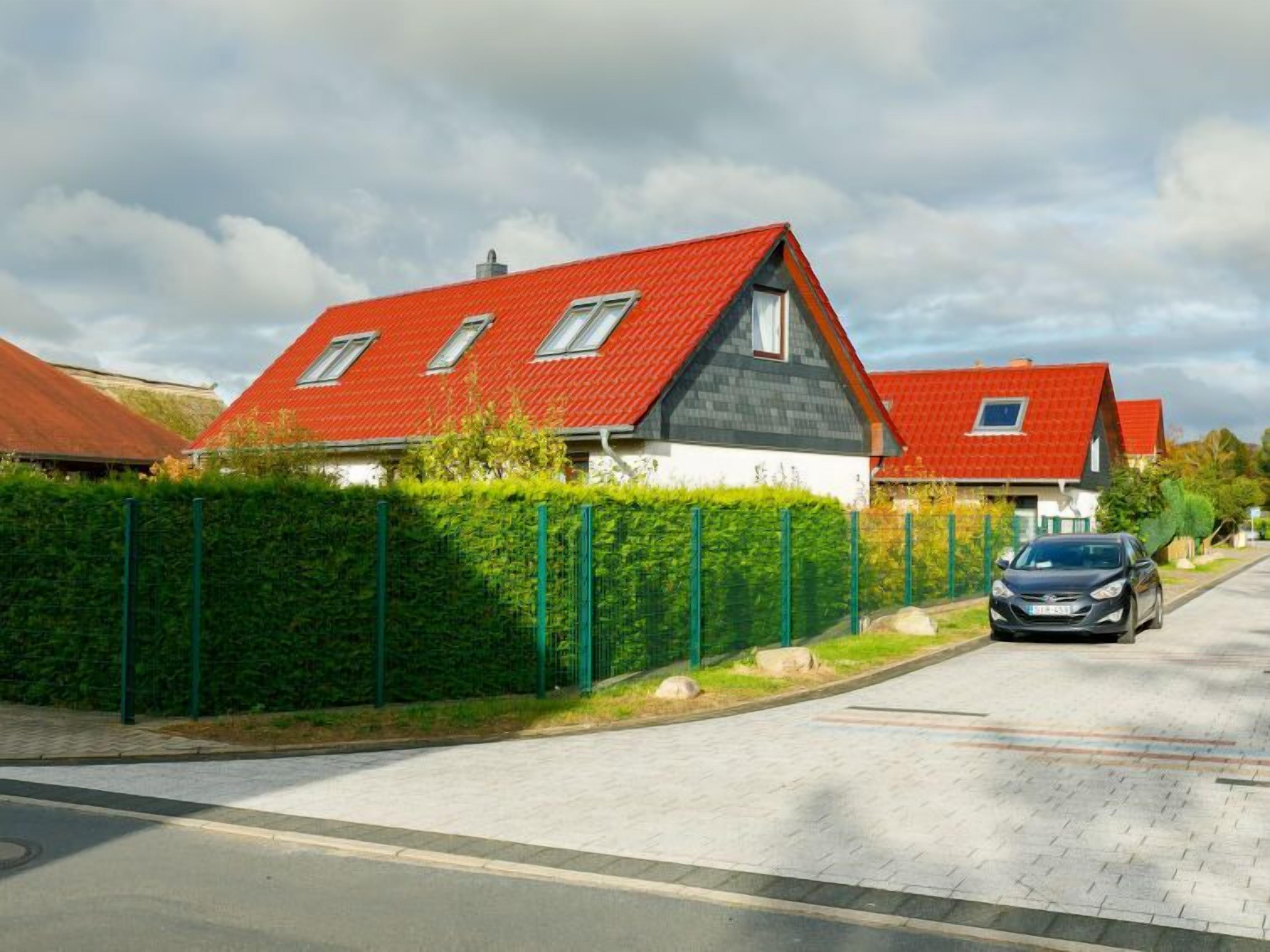A residential street with houses featuring red roofs and a car parked on the side.
