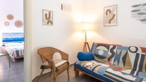 A room with a wicker chair, a colorful sofa, and a bed with striped bedding. There are wall-mounted lamps and framed artwork. - Il Giglio by Interhome (Scarlino)