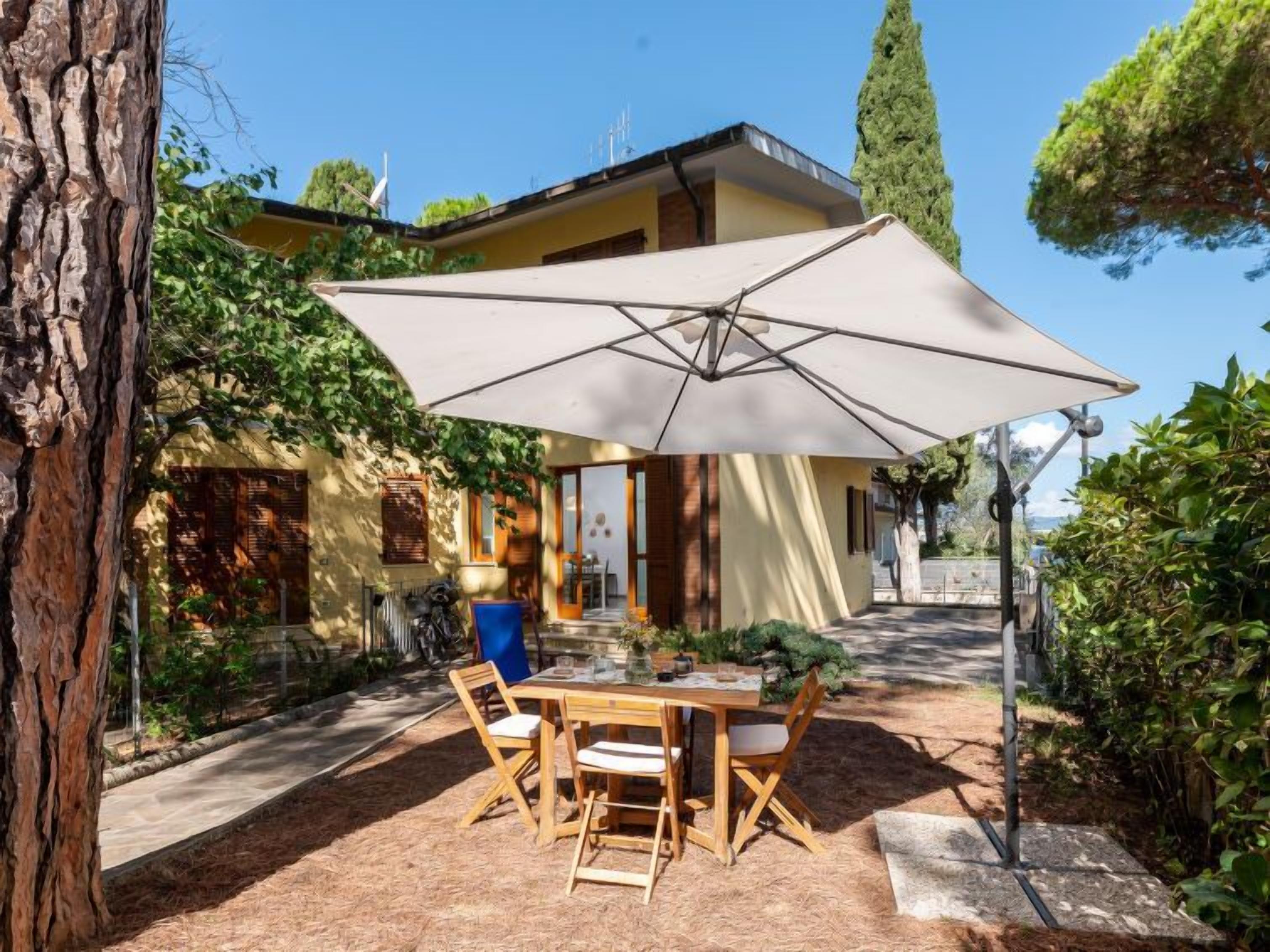 Un patio con una mesa y sillas, un paraguas y vistas a un edificio de fachada amarilla y un árbol.