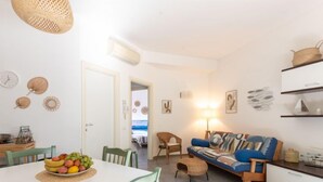 A bright living room with a white sofa, a dining table with fruit, and a view to the outside. - Il Giglio by Interhome (Scarlino)