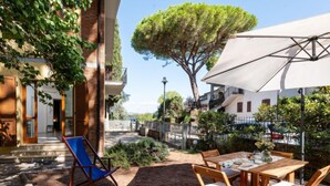 An outdoor patio with a table and chairs, surrounded by a garden and a large tree. - Il Giglio by Interhome (Scarlino)