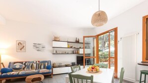 A modern living room with a sofa, dining table, chairs, and a large window. - Il Giglio by Interhome (Scarlino)