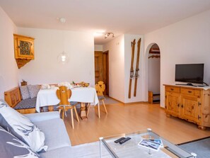 A living room with a sofa, dining table, chairs, a TV on a wooden cabinet, and skis leaning against the wall. - Chesa Palüdin 10 - Pontresina by Interhome (Pontresina)