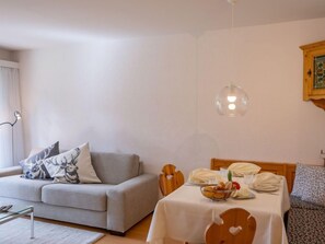 A modern living room with a grey sofa, a dining table set for two, and a hanging light fixture. - Chesa Palüdin 10 - Pontresina by Interhome (Pontresina)
