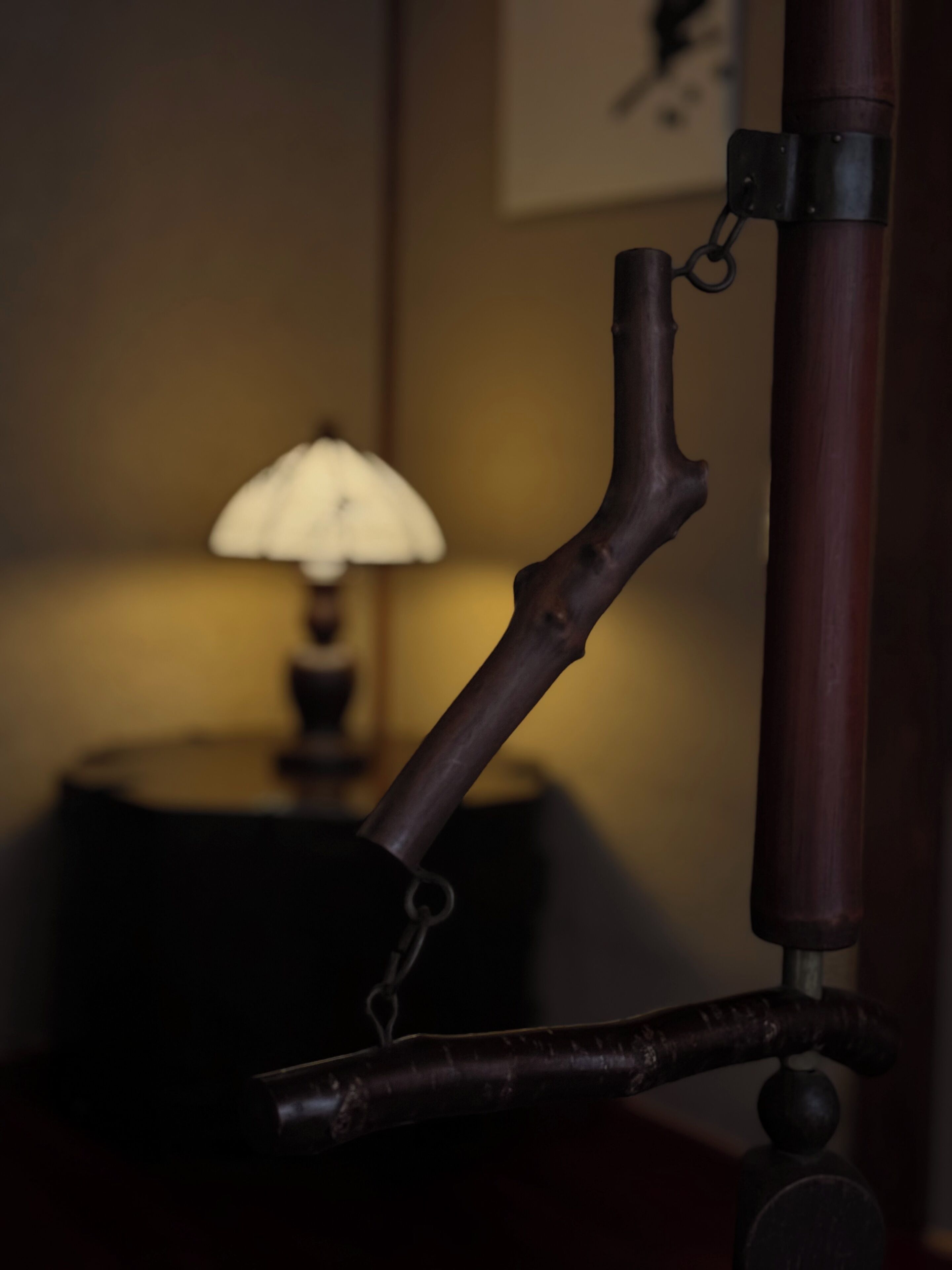 A close-up of a wooden object with a curved handle, possibly a part of furniture or a decorative item, in a dimly lit room with a lamp in the background.