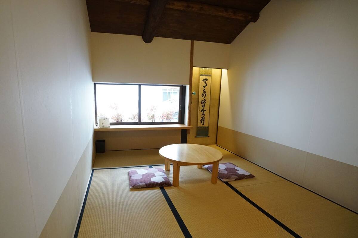 Een kamer met tatami matten, een lage tafel en kussens, een raam en een wandlamp.