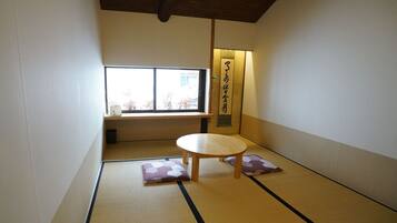 Une pièce avec un sol recouvert de tatamis, une petite table basse et des coussins, une fenêtre et un luminaire fixé au mur.