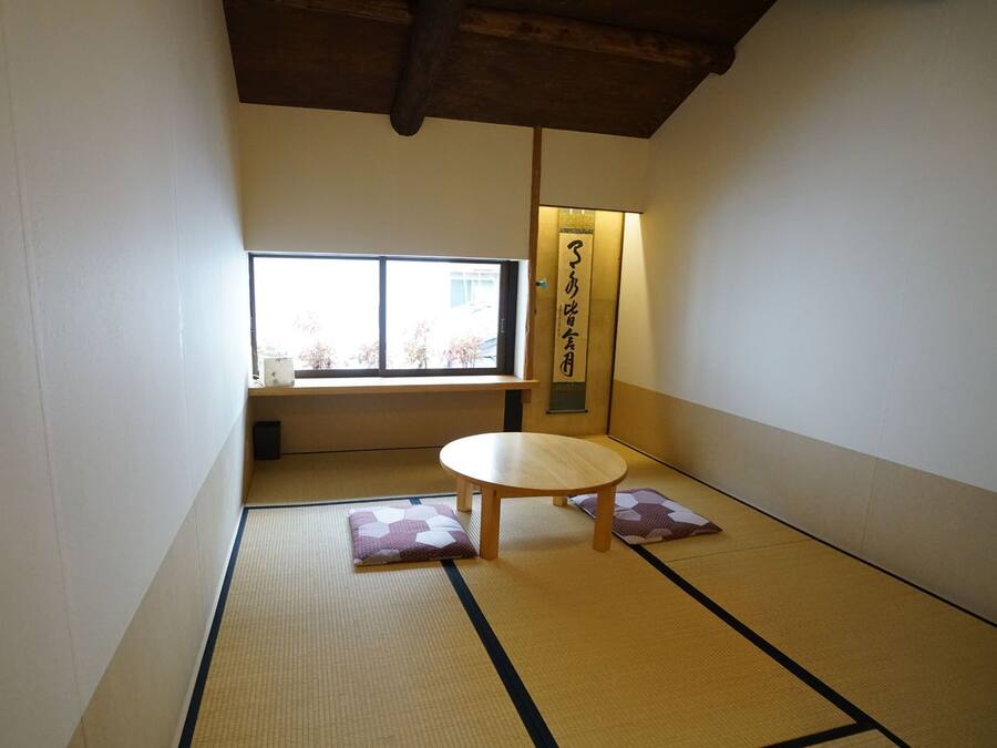 Une pièce avec un sol recouvert de tatamis, une petite table basse et des coussins, une fenêtre et un luminaire fixé au mur.