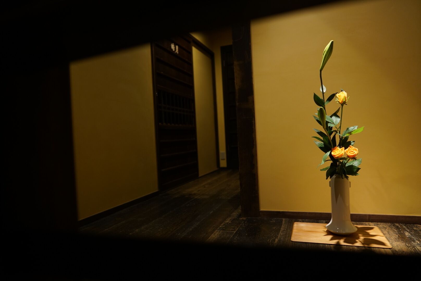A hallway with a white vase containing yellow flowers on a wooden table.