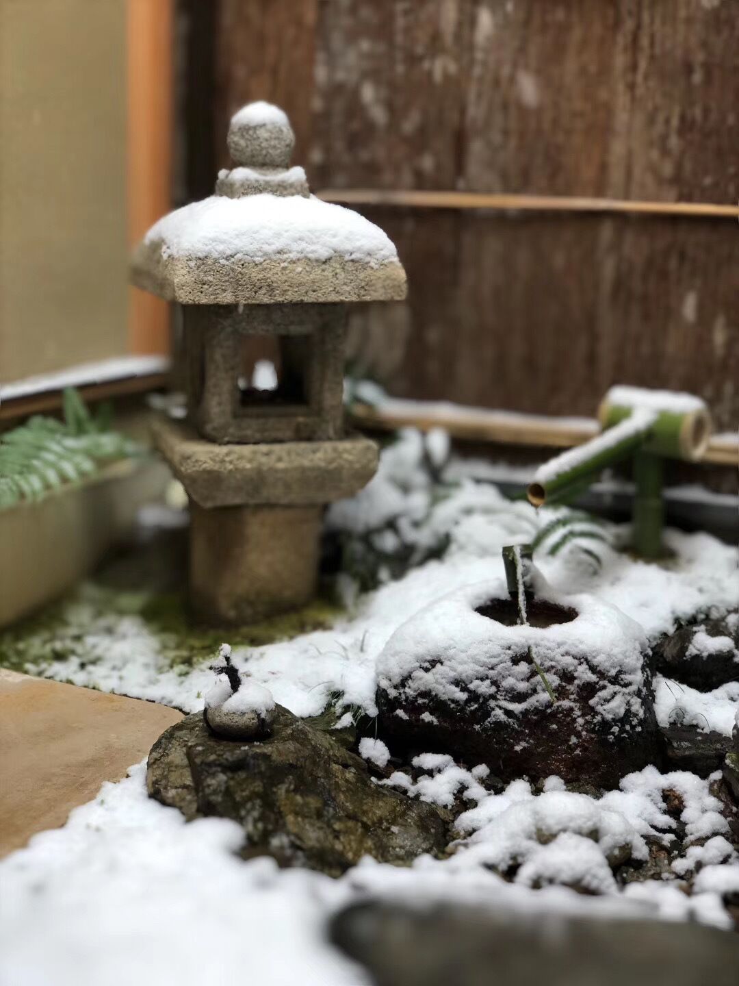 Ein aus Stein gefertigter Laternenstock, bedeckt mit Schnee, umgeben von Steinen und einer kleinen Gartenanlage.