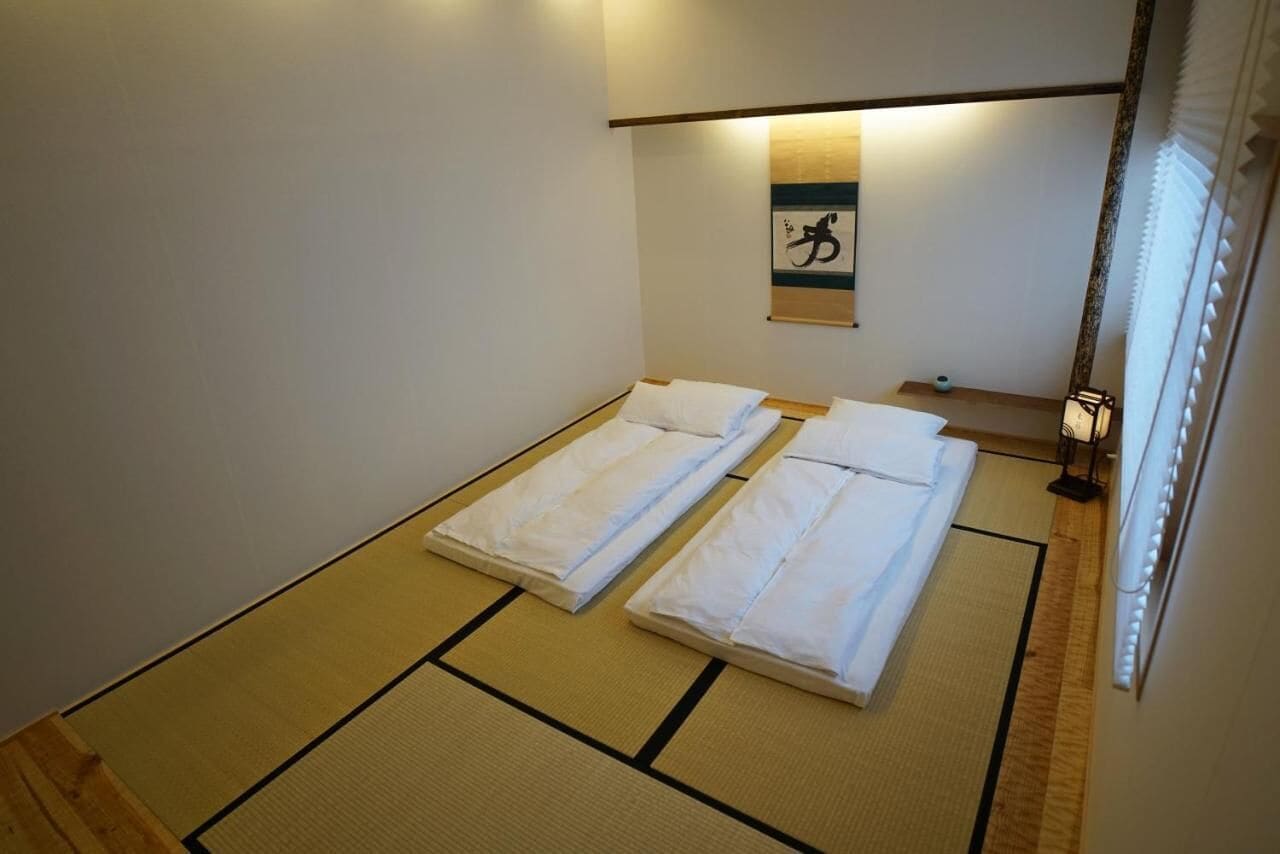 Une chambre avec deux lits, des tatamis, une œuvre d’art accrochée au mur et une table de chevet avec une lampe.