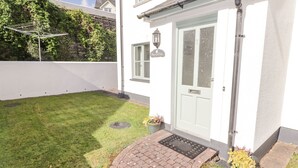 Une maison blanche avec une porte d’entrée, un petit jardin et un chemin de briques menant à la porte.