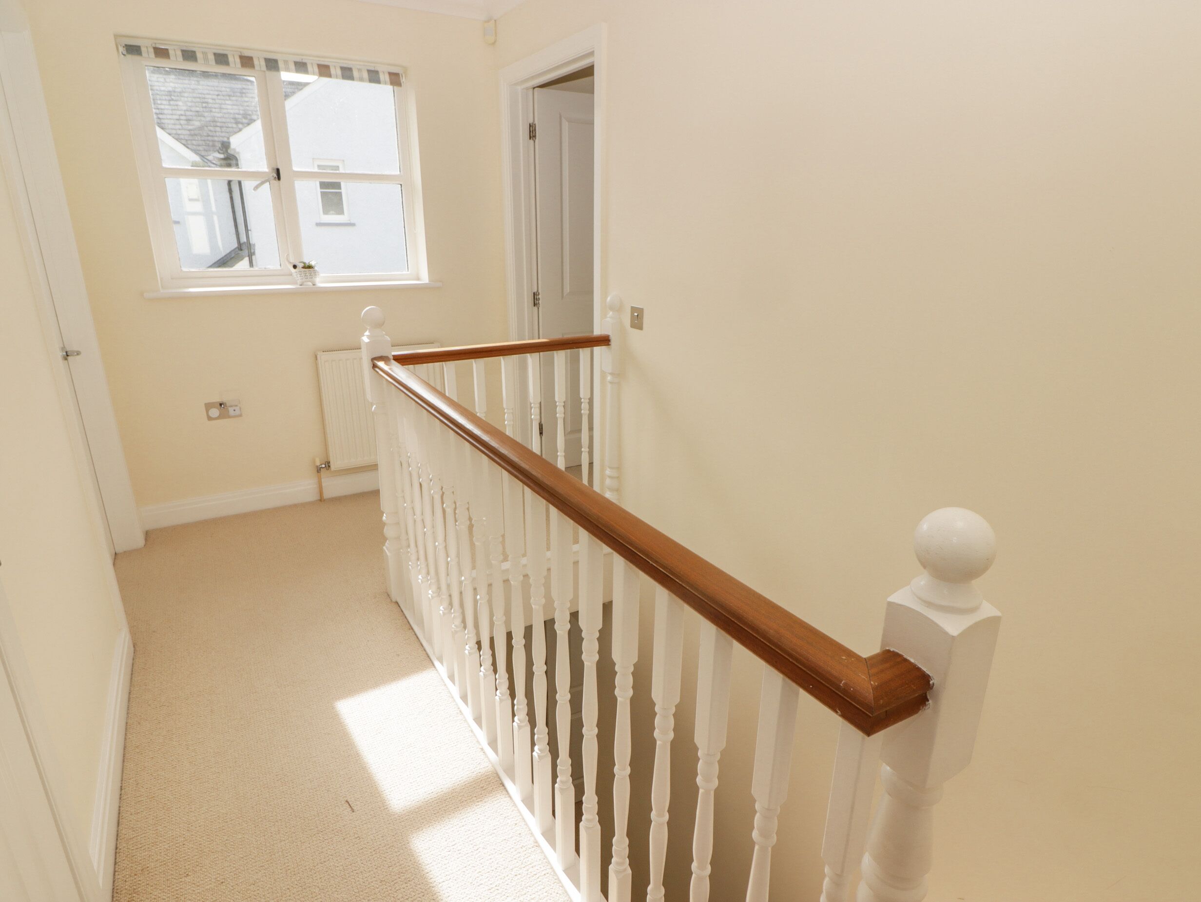A hallway with a wooden staircase, white walls, a radiator, and a window with a view of a building outside.