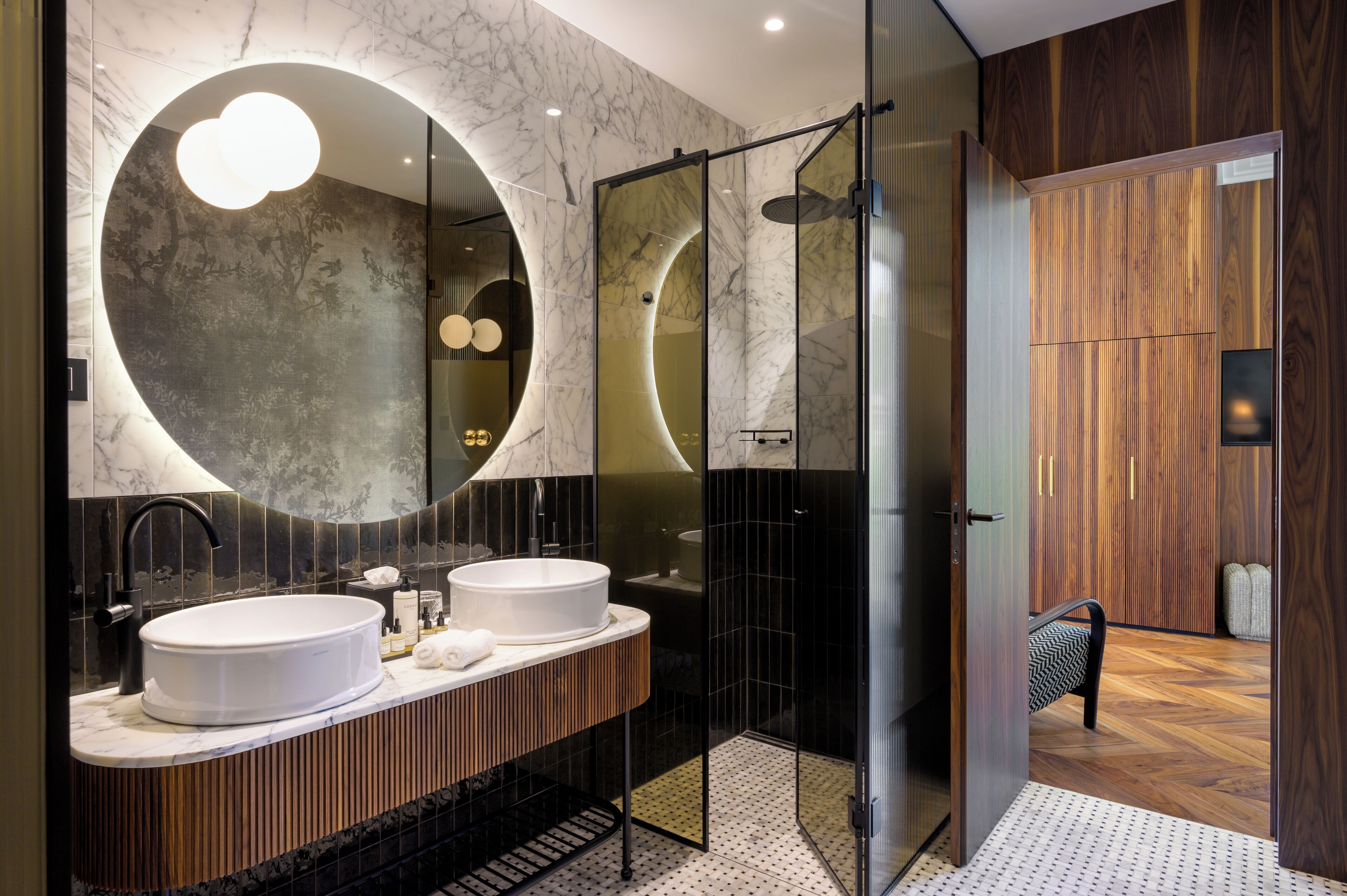 A modern bathroom with a large mirror, two sinks, and a walk-in shower.