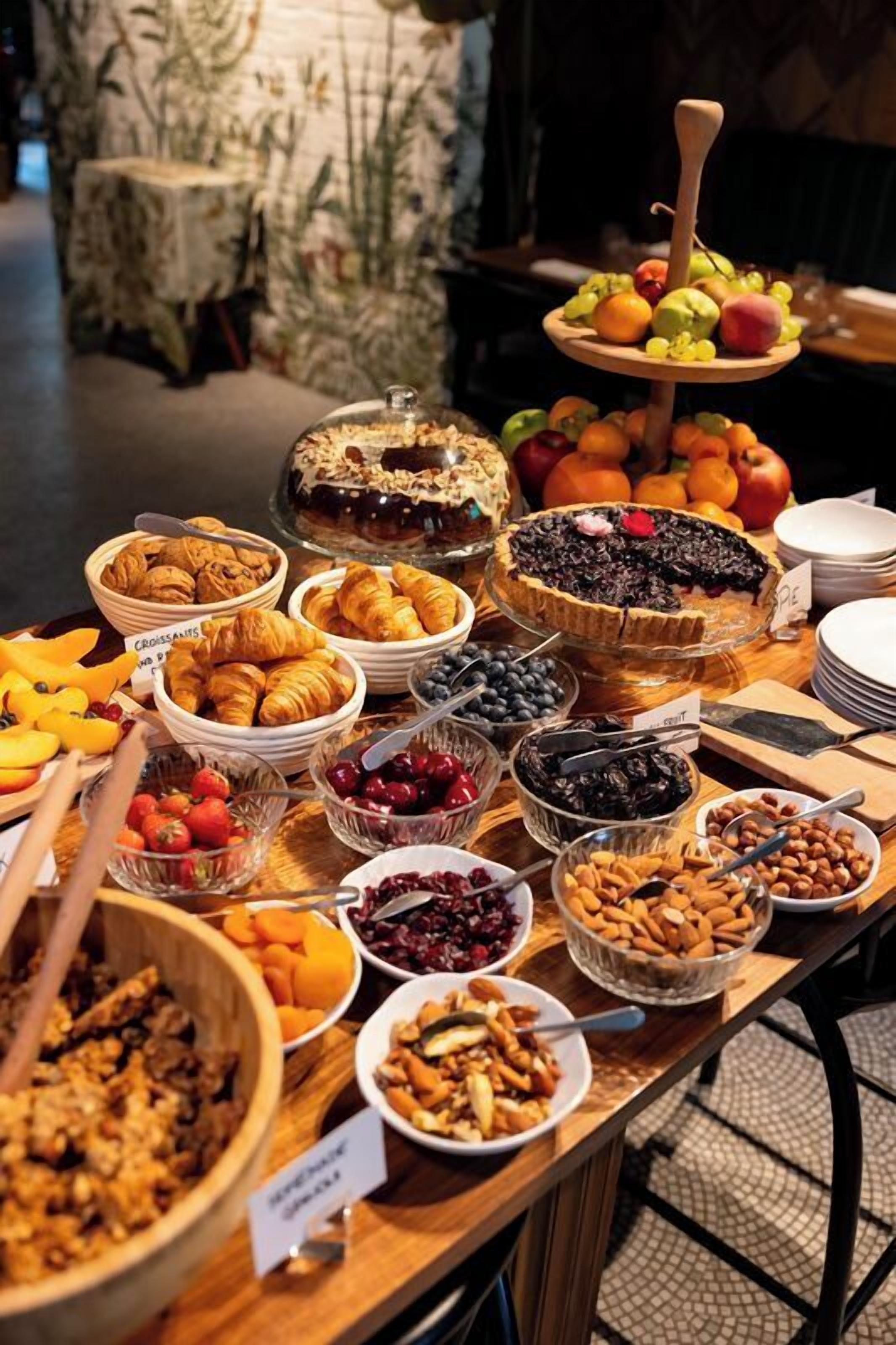 Une table de buffet proposant une variété d’aliments, notamment des fruits, des pâtisseries et des desserts.