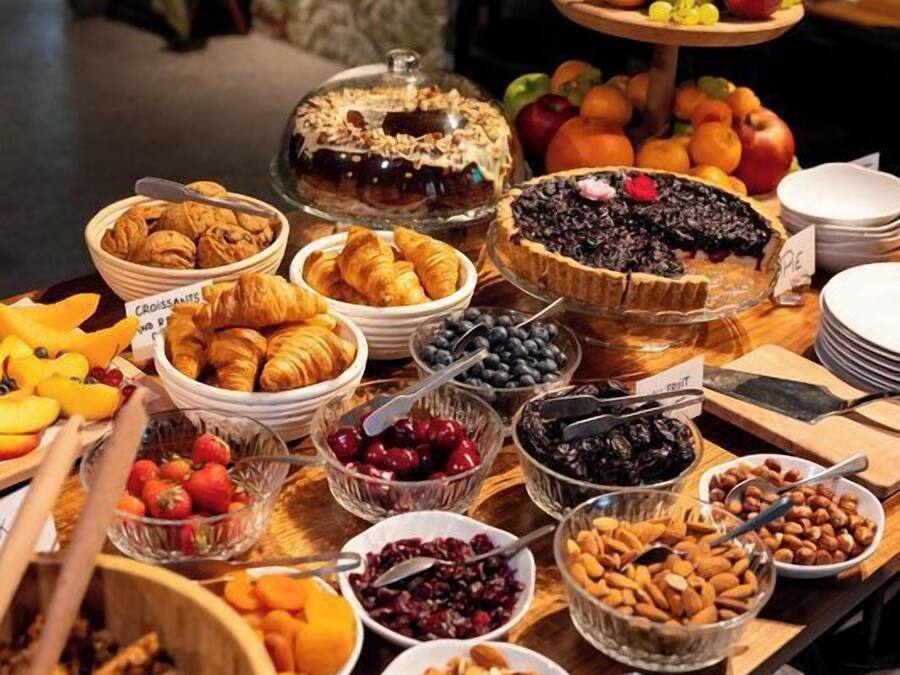 Une table de buffet proposant une variété d’aliments, notamment des fruits, des pâtisseries et des desserts.