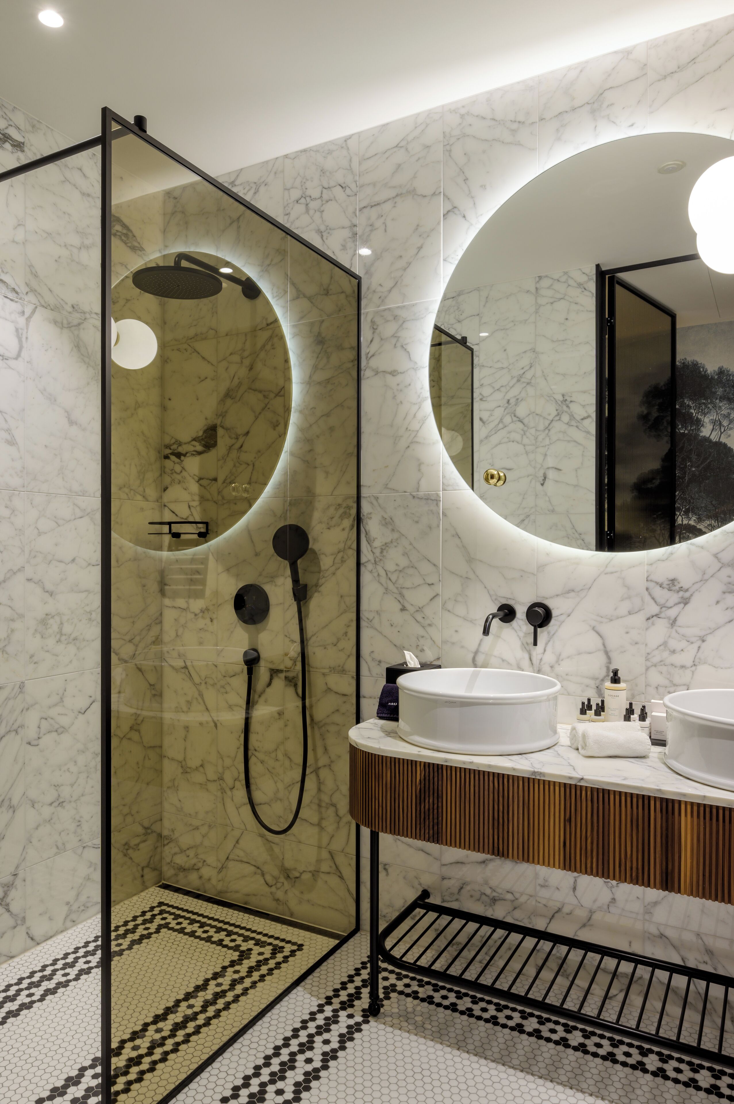 A modern bathroom with a glass-enclosed shower, marble walls, and a wooden vanity with two sinks.