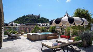 A rooftop terrace with lounge chairs, a hot tub, and umbrellas.