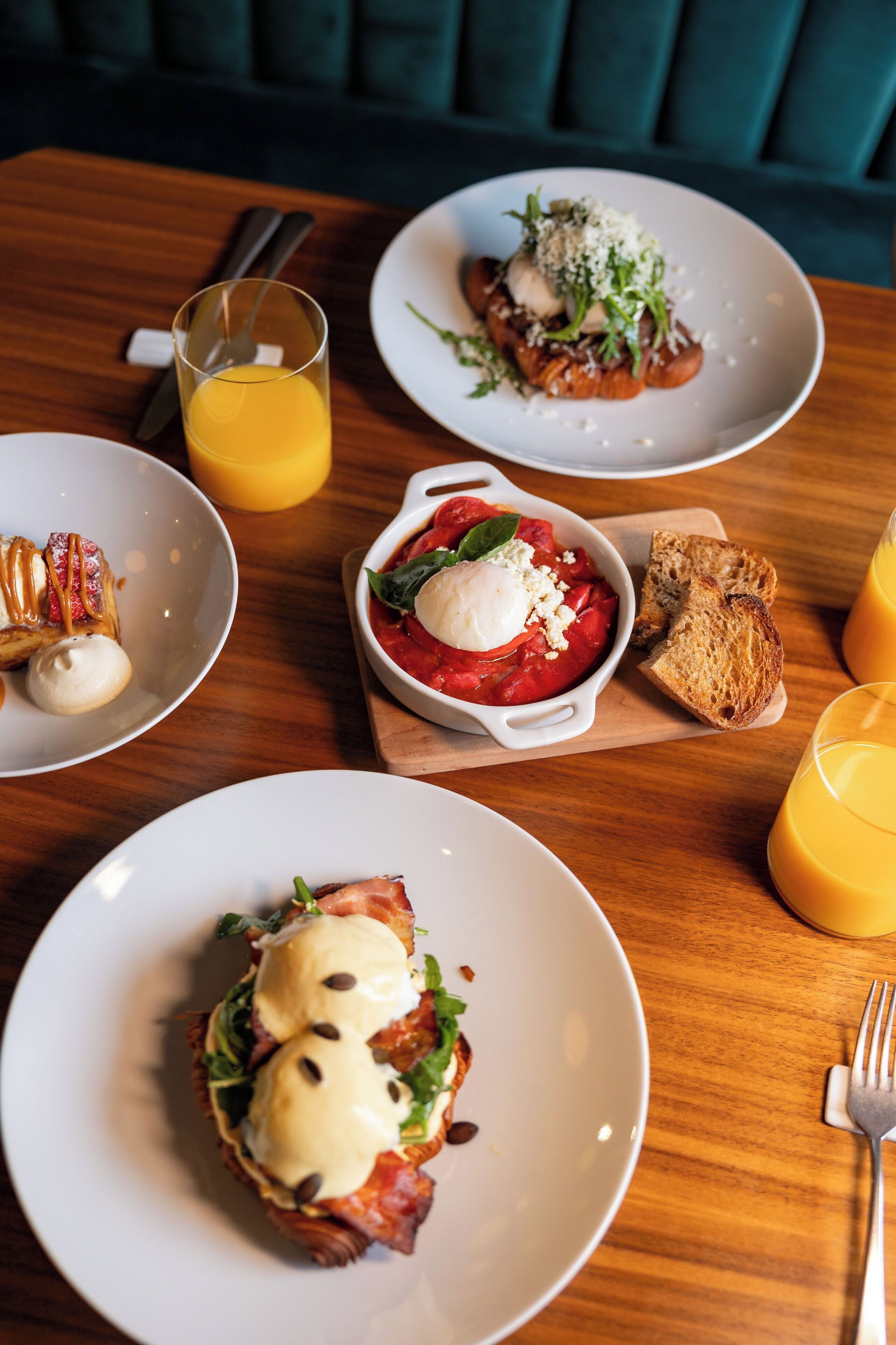 Desayuno con diferentes platos, incluyendo huevos, tostadas y un vaso de zumo de naranja.