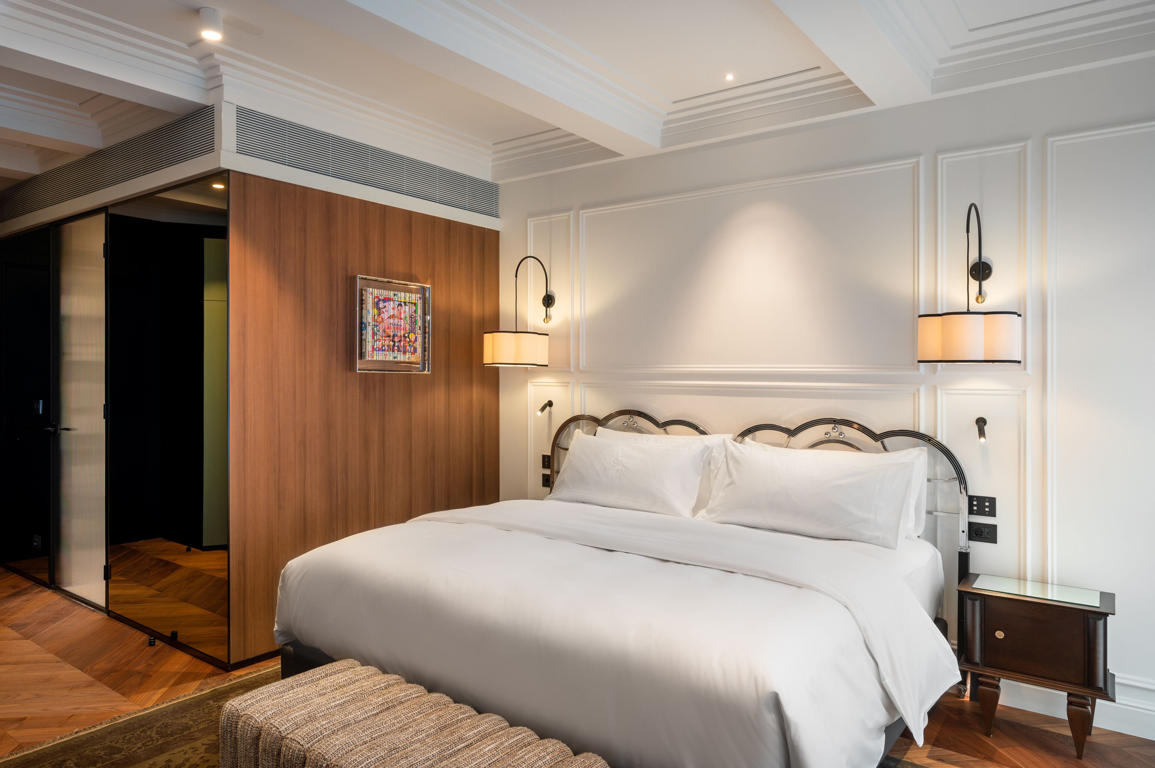 A neatly made bed with white linens, a wooden headboard, and two bedside lamps.