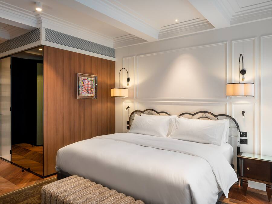 A neatly made bed with white linens, a wooden headboard, and two bedside lamps.