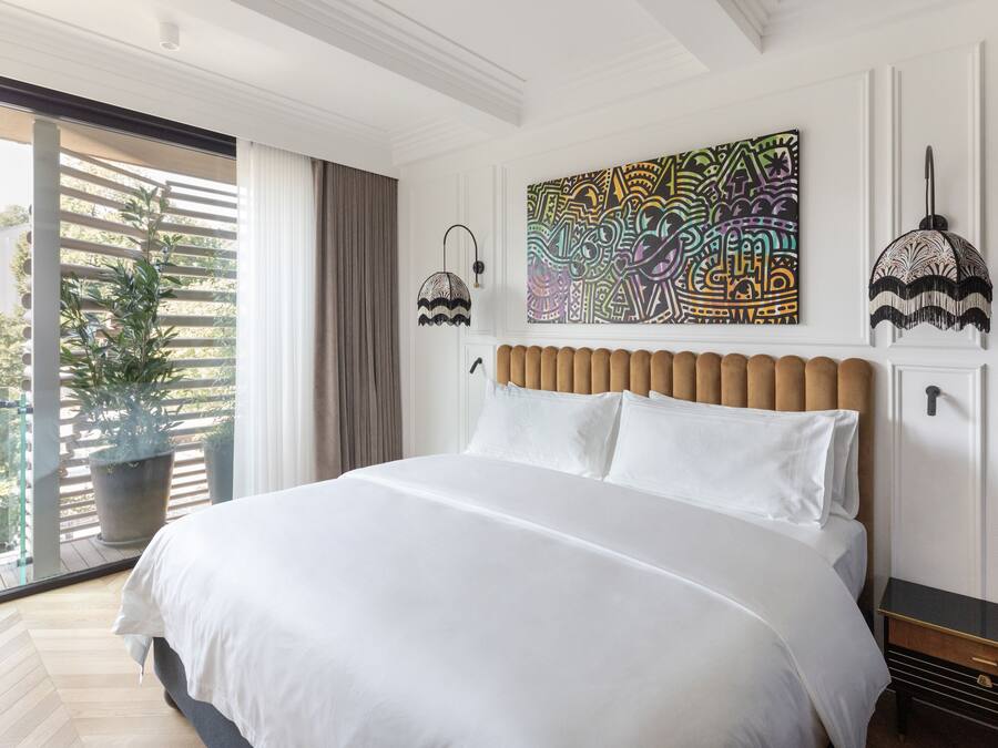 Une chambre moderne avec un grand lit, une vue sur la verdure et un tableau abstrait aux couleurs vives accroché au mur.