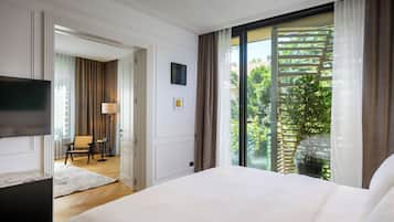 A hotel room with a large bed, a flat-screen TV, a desk, and a view of greenery through a sliding door.