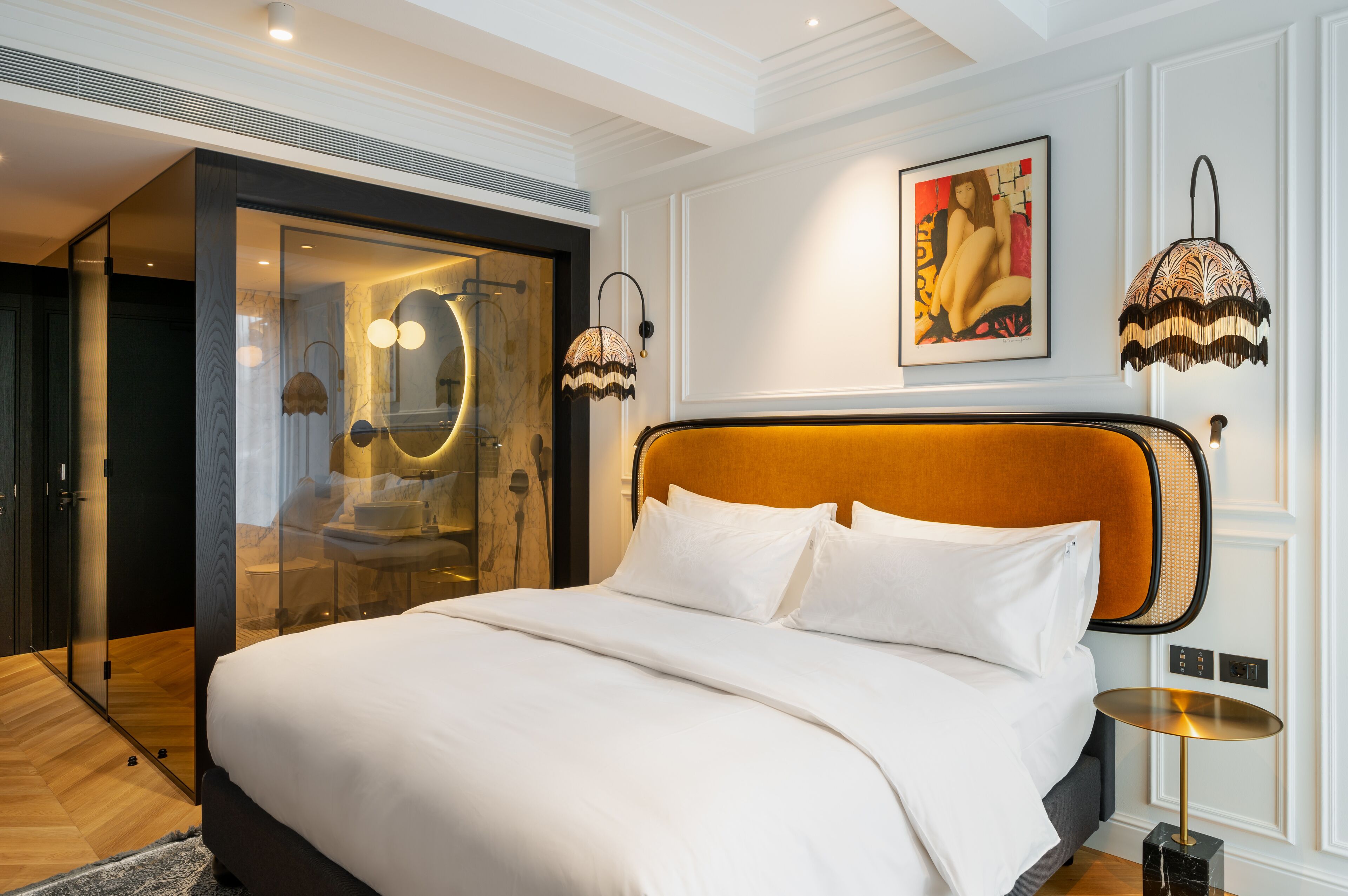 A modern hotel room with a large bed, a glass-enclosed walk-in closet, and a painting on the wall.