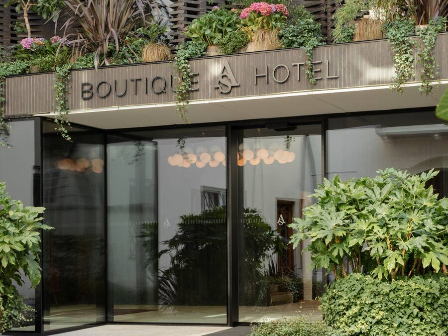 En hotelindgang med moderne design, med en glasfacade og en tagterrasse med forskellige planter.