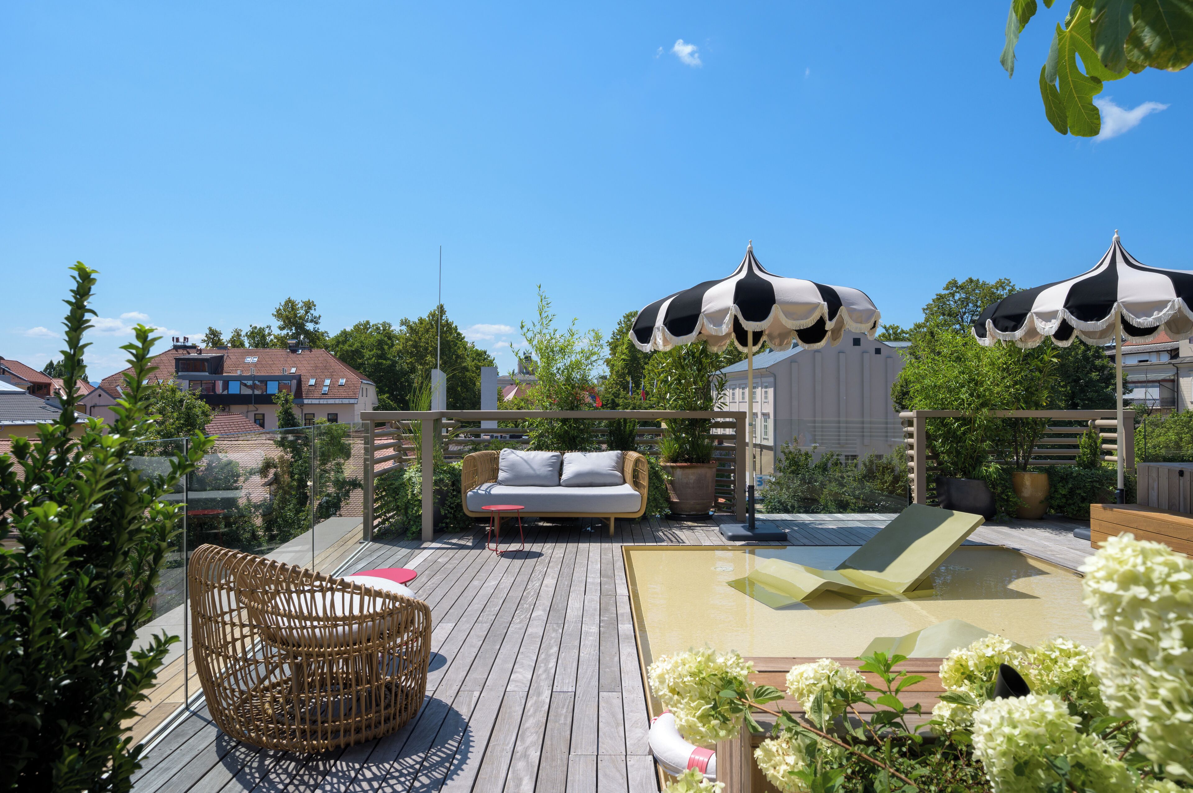 A rooftop deck with a wicker chair, a sofa, and two black and white umbrellas.