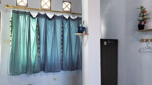 A room with teal curtains, a potted plant, and a shelf with a hanging bag. - Hans Yoga Homestay (Kuta)