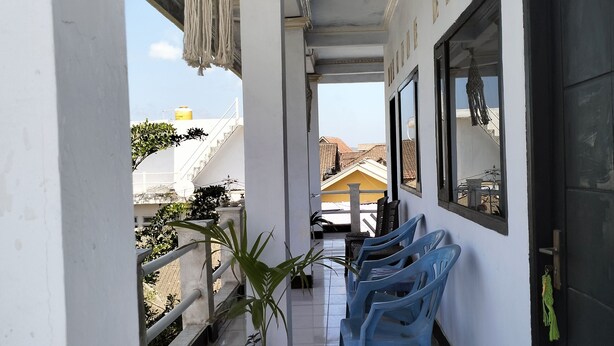 A balcony with blue plastic chairs, a potted plant, and a view of neighboring buildings. - Hans Yoga Homestay (Kuta)