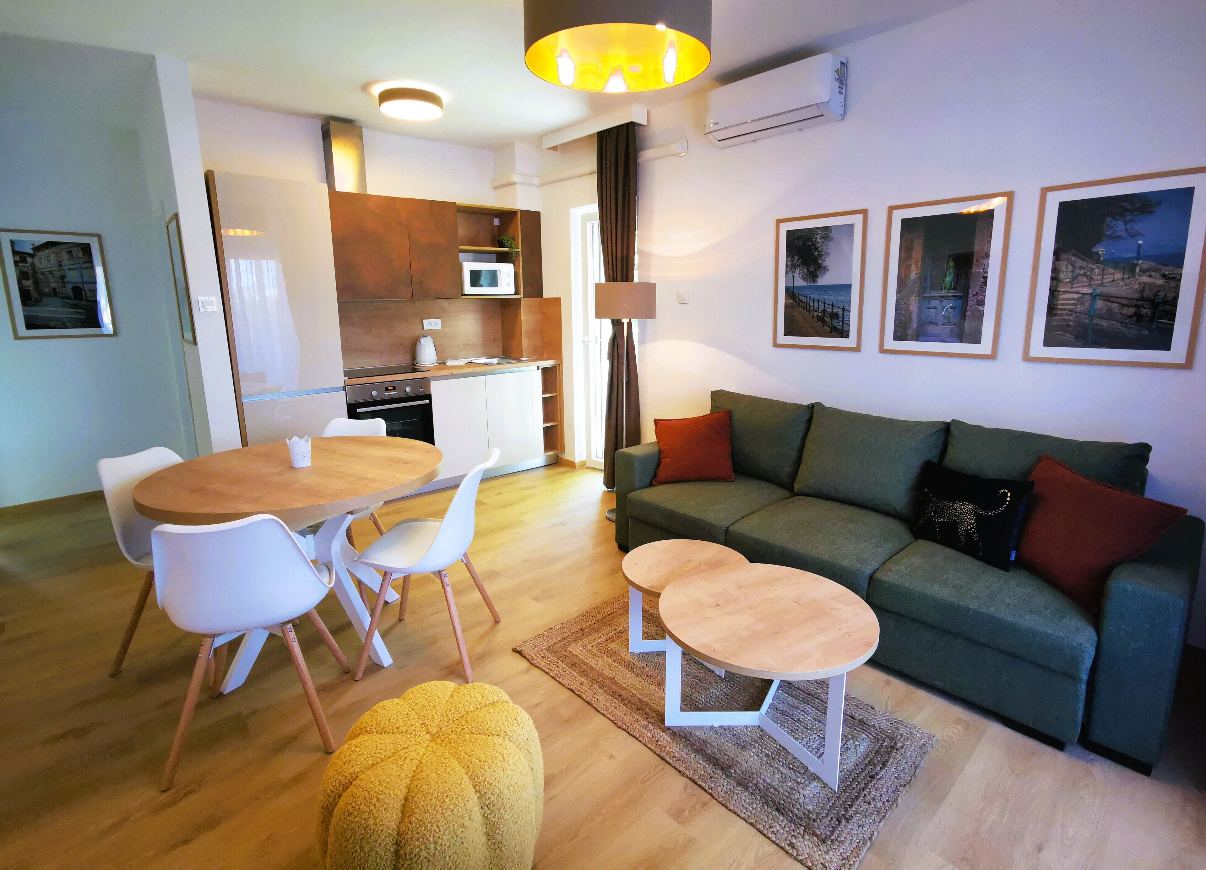 A modern living room with a green sofa, a wooden dining table with chairs, and a small round table.