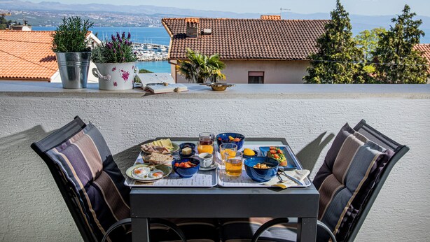 Une table à manger avec une batterie de table, des chaises et une vue sur la mer et les bâtiments en arrière-plan.