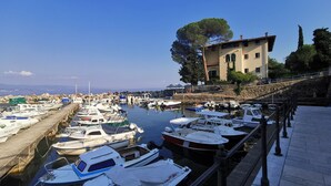 Un port de plaisance où sont amarrés différents types de bateaux, un mur de pierre et un bâtiment situé à proximité d’un arbre.